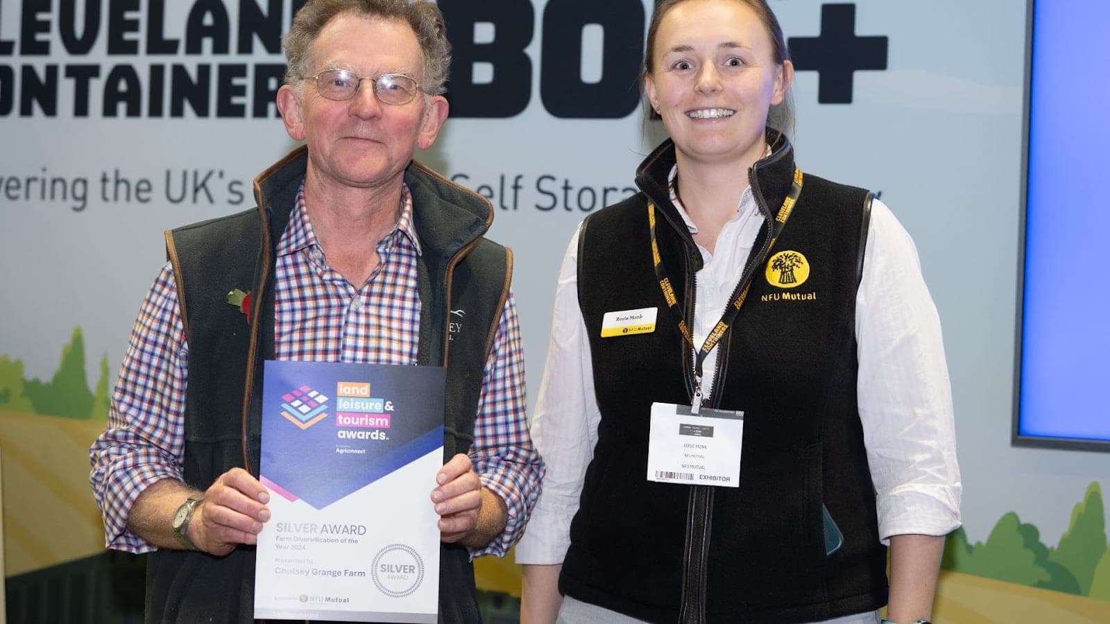 Ted receiving a framed award certificate at the Farm Business Innovation Show, standing beside a presenter in front of exhibition banners.