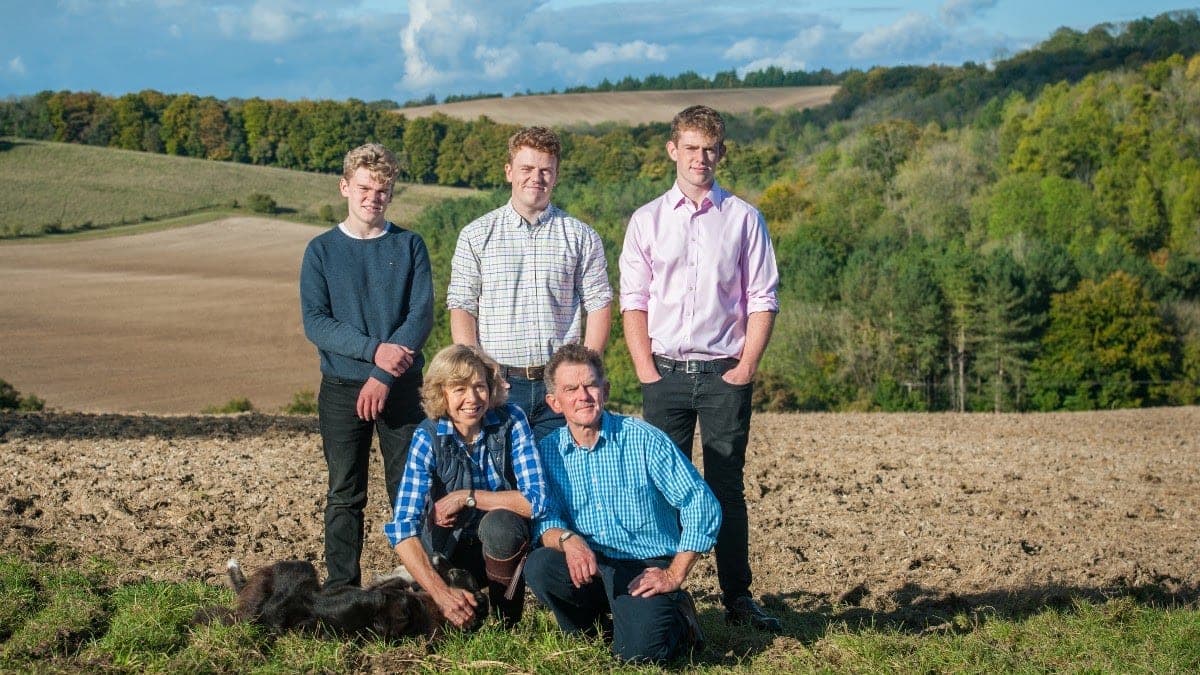 The Howard-Jones family standing and sitting together in a ploughed field, with the wooded Chiltern valley behind them.