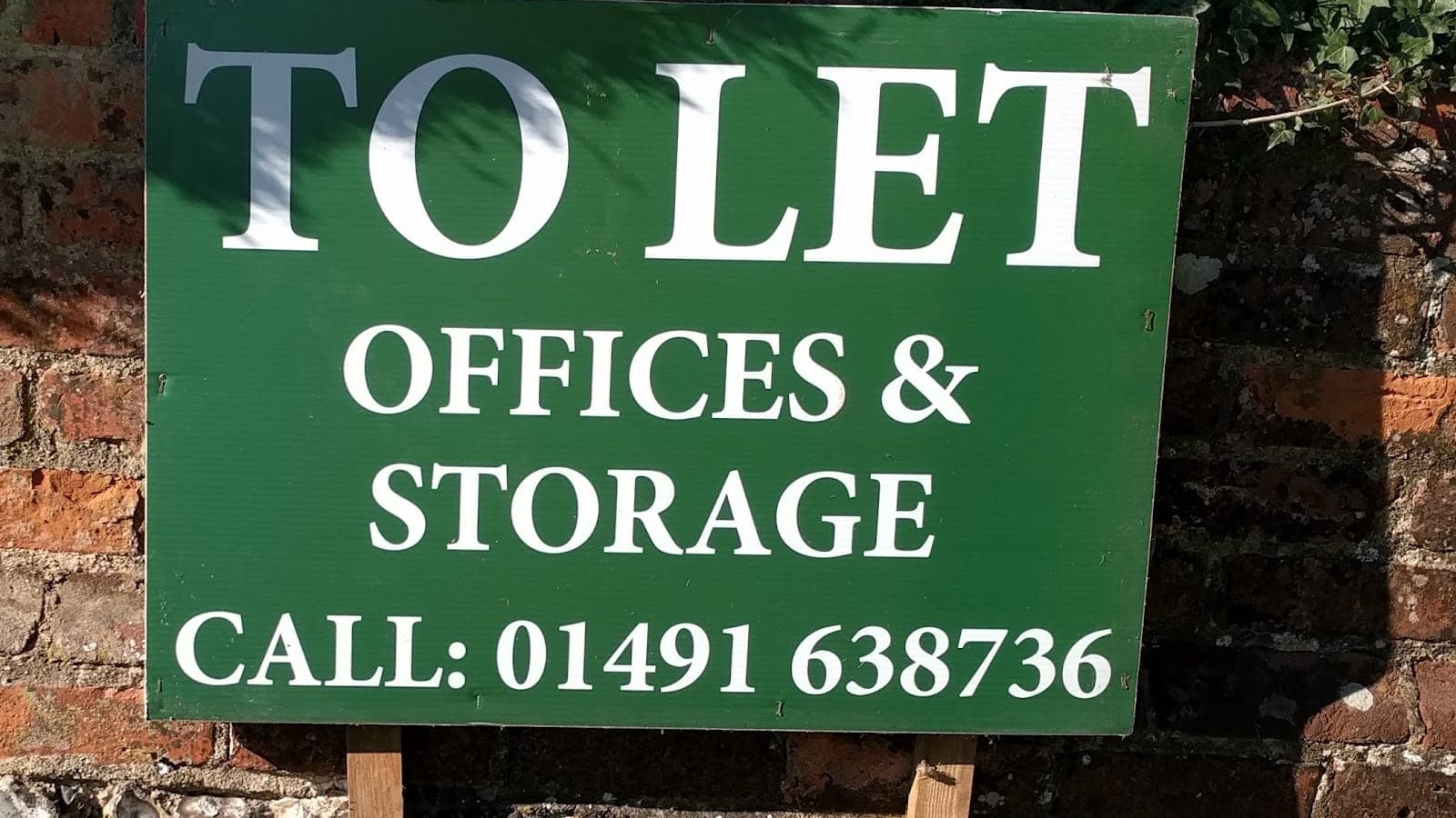 A painted green sign on a brick wall reading 'To Let: Offices & Storage', with a telephone number beneath.